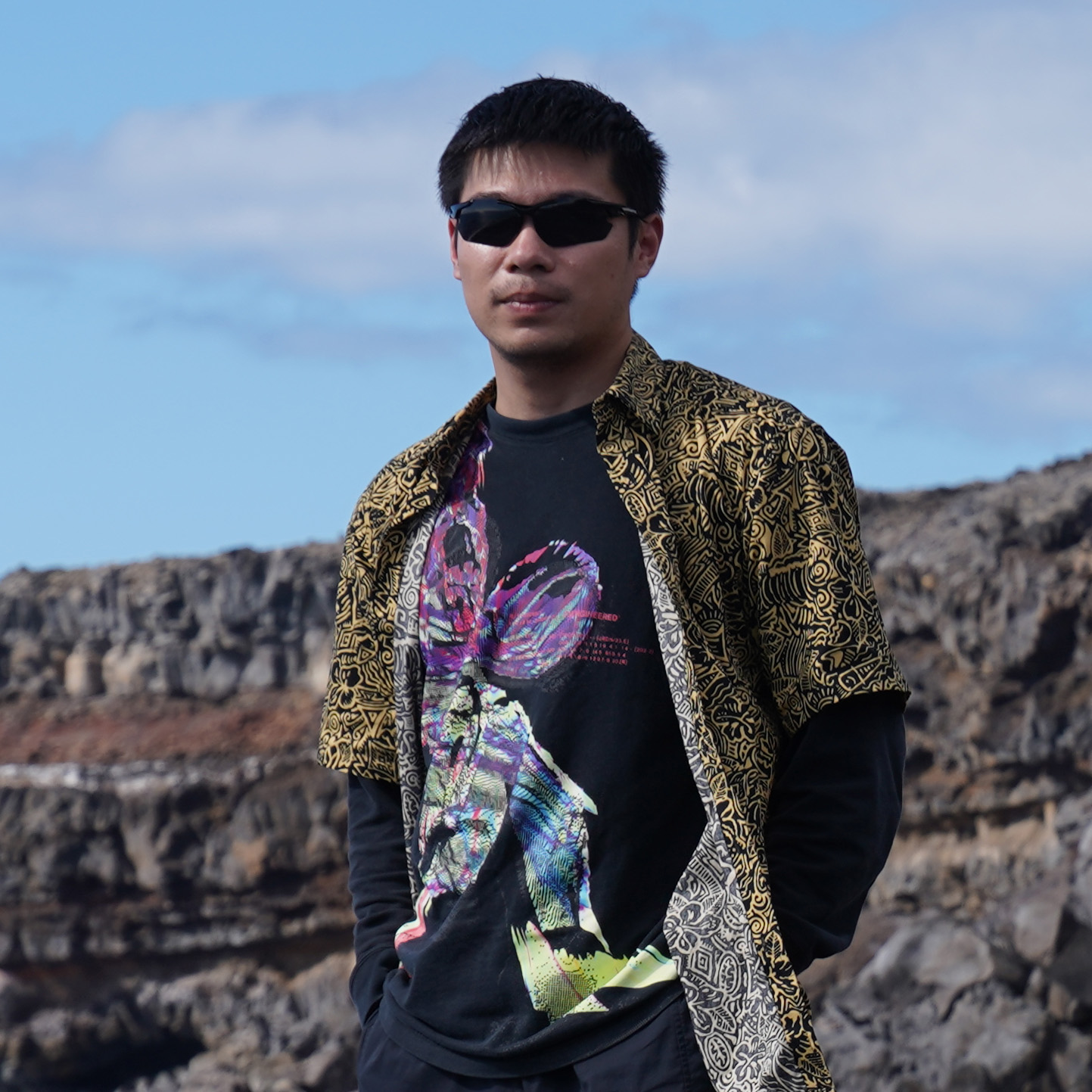 Portrait of Wei Yue standing outdoors against a rocky landscape.